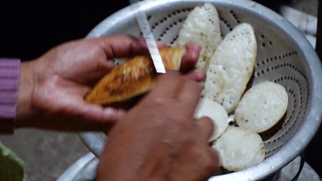 The burnt parts of the hot chitai pitha, made by mixing rice flour with water and salt, are cleaned with a knife. 