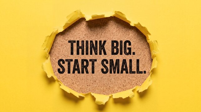 Think big start small motivational quote printed in black text upon brown cork surface visible through circular tear in bright vibrant yellow paper sheet revealing inspiration