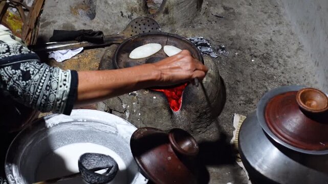A woman brings out the finished Chitai Pitha in a hot clay oven. Chitai pitha is being made in a terracotta mold for making pitha in a heated clay oven.