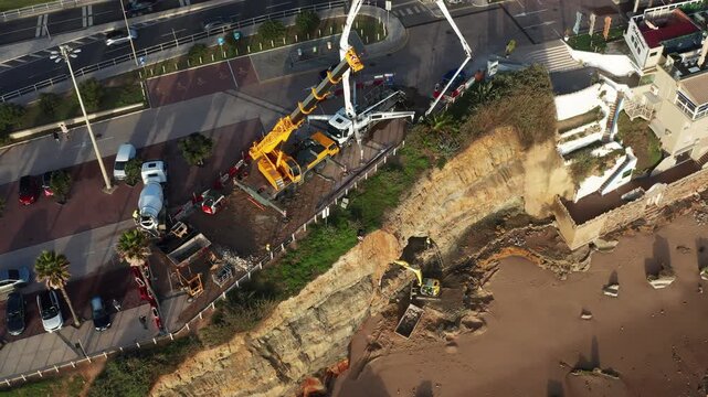 Workers and equipment are on Sao Pedro Estoril aerial view beach to address soil erosion. Heavy machines dig into the sand to prevent further damage along the beach area.