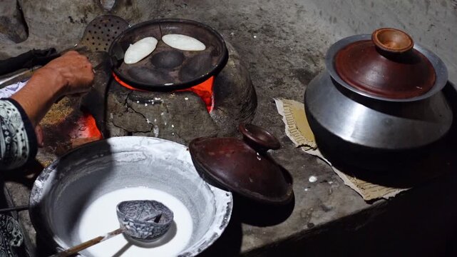 A woman brings out the finished Chitai Pitha in a hot clay oven. Chitai pitha is being made in a terracotta mold for making pitha in a heated clay oven.
