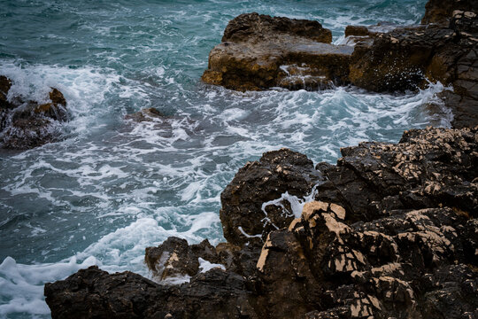 Turquoise sea waves splashing against a rocky coastal shore.