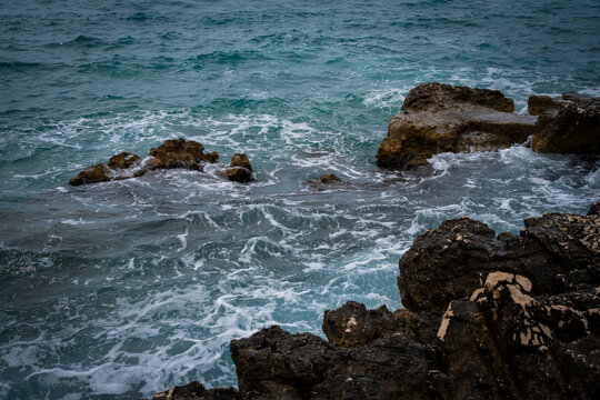 Sea waves splashing over dark rocky coast.