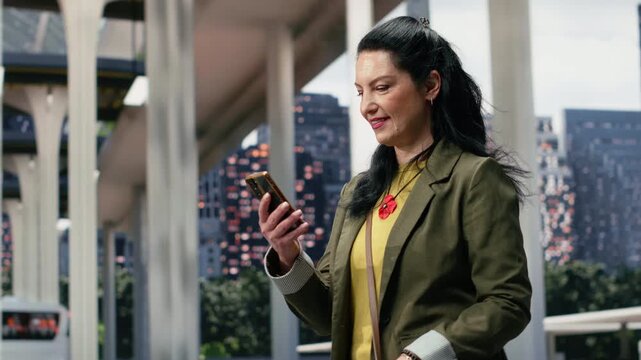 Female passenger reads travel updates on her smartphone inside the coach station, sending text messages while walking through the urban transport hub during a weekday commute before departure.