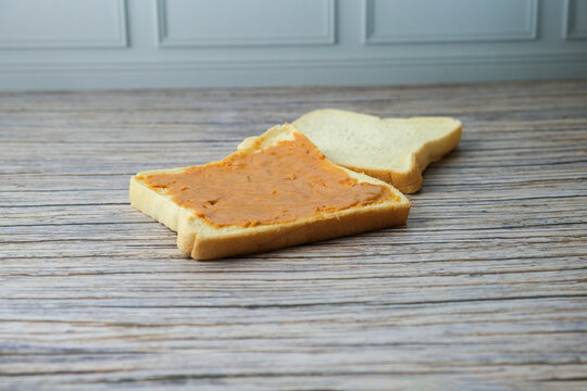 White breads with smooth peanut butter spread. Wooden surface shows gentle texture and natural grain. No people, no animals, no plants in this image. Ideal for breakfast, healthy eating