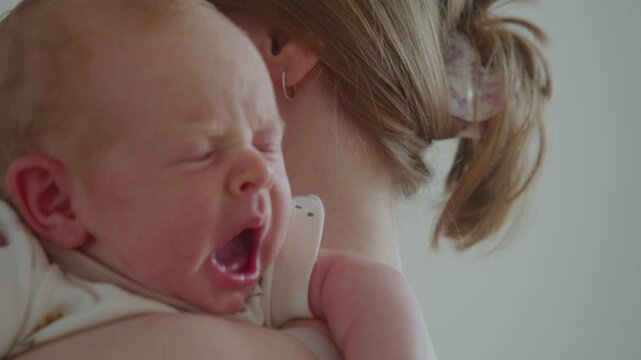 Baby yawns while resting on mother's shoulder after prolonged soothing. Sleepy reflex signals fading tension and approaching rest, with maternal warmth providing familiar place to relax.