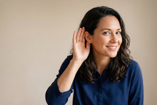 Smiling woman holds a hand to her ear to listen closely to a quiet sound or secret conversation