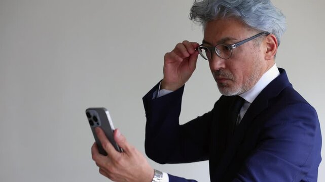スマートフォンの画面が見えにくい老眼のシニアビジネスマン