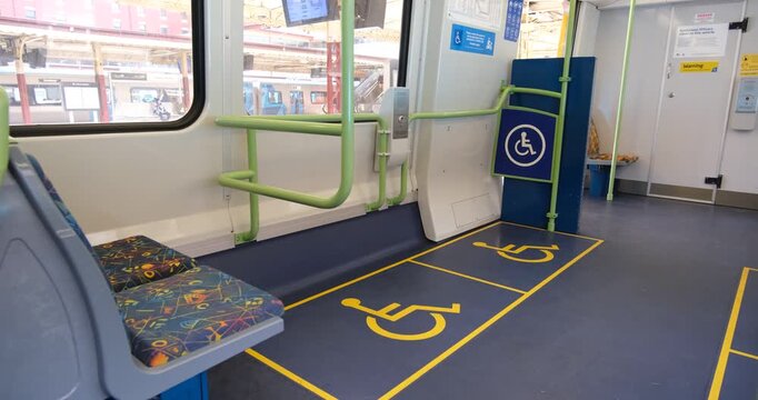 An empty train carriage with a dedicated wheelchair-accessible bay with floor decals and priority grab rails.&nbsp;Station platforms are visible through the large windows. Melbourne, Australia.