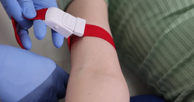 Doctor applying medical tourniquet on patient's arm indoors, closeup