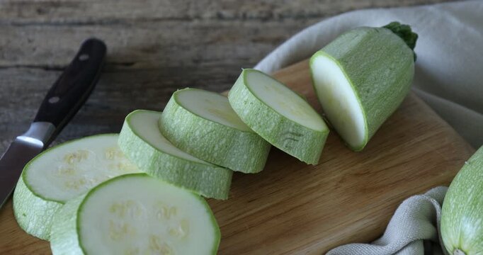 Pieces of fresh zucchini and knife on wooden table, closeup. Camera moving in