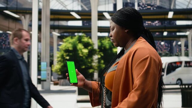 Woman checks a travel schedule on a chroma key phone in a city bus terminal; the passenger reviews route information on the isolated screen before departure.