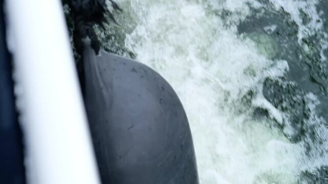 Black rubber fender on boat side splashes water as vessel moves through waves, creating foam and ripples in the water, showcasing maritime activity and movement