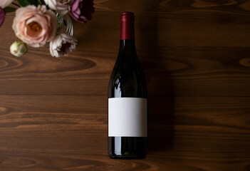 Obraz premium Red wine bottle with blank label and flowers on a dark wooden table, top view for branding and celebration concepts