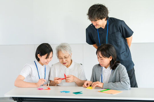 Elderly people, including senior women and male and female caregivers, do origami at a group home/nursing home.