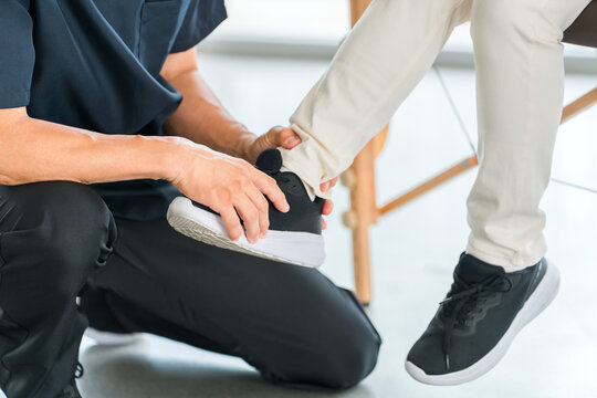 A senior woman receiving rehabilitation treatment for a foot injury at a hospital orthopedics department, along with a doctor and physical therapist.