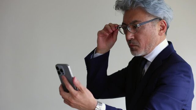 スマートフォンの画面が見えにくい老眼のシニアビジネスマン