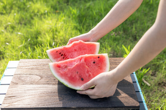 Hands placing sliced watermelon on wooden table outdoors in grassy field