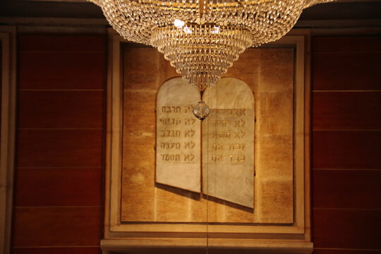 Luxurious crystal chandelier hanging in front of Hebrew Ten Commandments tablets in a synagogue