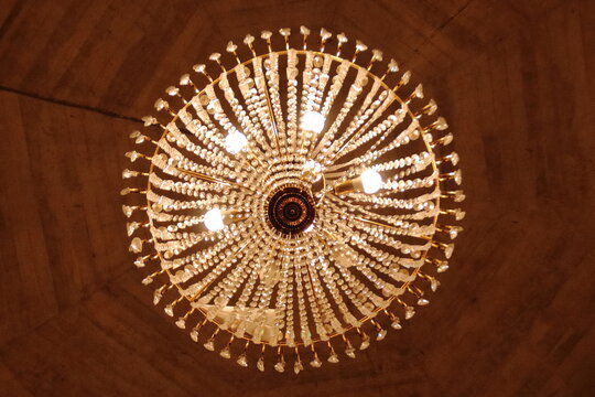 Bottom-up view of a large luxurious crystal chandelier with glowing warm lights.