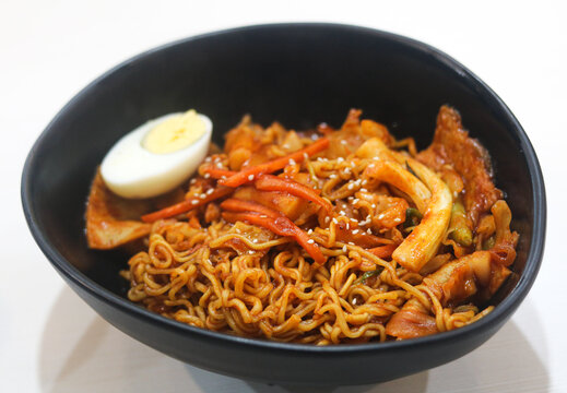 Korean street food Rabokki, spicy ramyeon noodles with tteokbokki rice cakes, fish cake, vegetables, and boiled egg served in a black bowl.