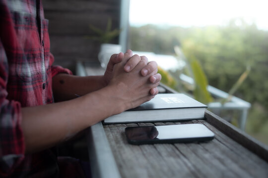 Close up of a man praying, hands clasped together on Bible, devotional concept.