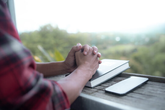Close up of a man praying, hands clasped together on Bible, devotional concept.