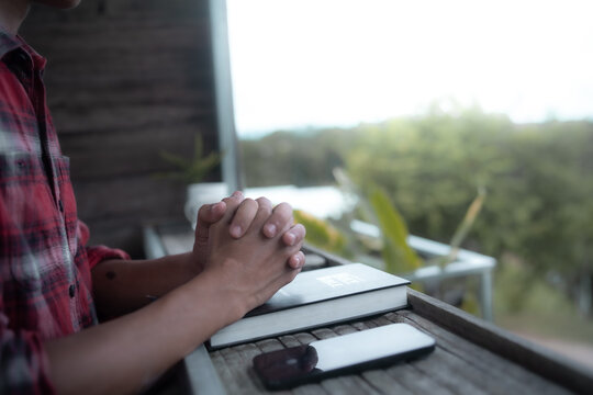 Close up of a man praying, hands clasped together on Bible, devotional concept.