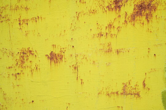Rusty bright yellow metal texture background closeup. Weathered corroded iron surface with brown rust spots, scratches, and peeling paint layers.