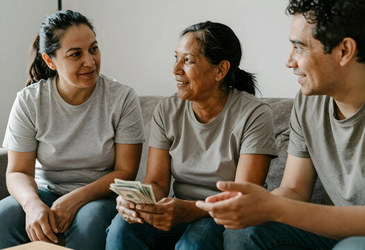 Multi-generational family discussing finances and money management at home, financial planning and savings concept, an older woman holds cash while conversing with a younger woman and a man