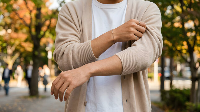 Close-up of a young person putting on a lightweight cardigan over a summer shirt outdoors