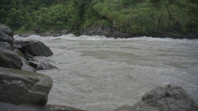 Mid-shot focused on swirling gray-brown water creating fast ripples and foam along a natural river channel