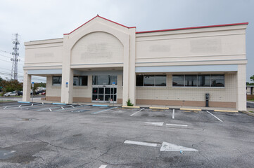 Fototapeta premium Empty vacant storefront in a closed retail building with an abandoned parking lot and overcast sky, conveying urban decay, economic decline and quiet commercial isolation in a suburban shopping center