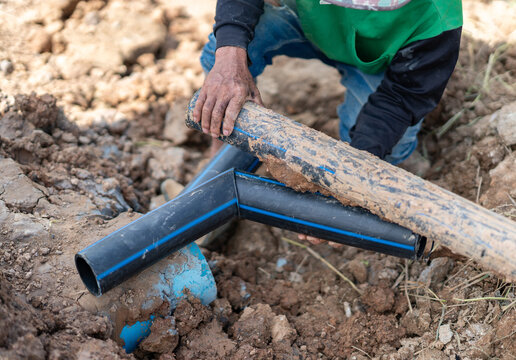 Close-up of a worker's hands aligning HDPE plastic piping and fittings inside an excavated trench on a construction site.