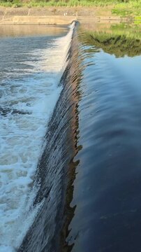 Fast-flowing water rushing over a small dam structure, creating white foam, turbulent currents, and dynamic cascades that highlight the power and movement of flowing water