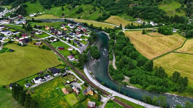 Aerial top down reveals a small Flam village with winding Flamselvi river railway line houses and patchwork farm fields in Norway
