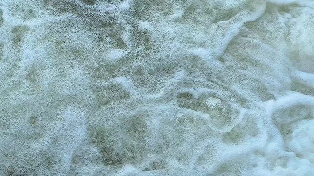 Turbulent water swirling and churning with foamy bubbles and dynamic ripples, creating a dramatic natural texture that captures the movement, energy, and fluid patterns of flowing water.