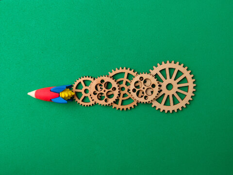 A toy rocket pointing left connected to a line of five wooden gear cogs on green background