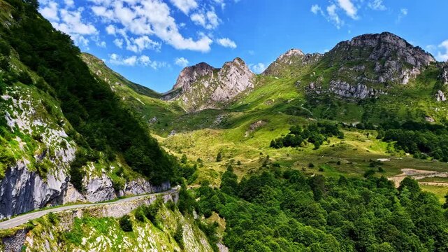 Rocky peaks rise above green valley as narrow cliffside road winds through Cirque du Litor high in the Pyrenees mountains