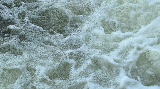 Turbulent water swirling and churning with foamy bubbles and dynamic ripples, creating a dramatic natural texture that captures the movement, energy, and fluid patterns of flowing water.