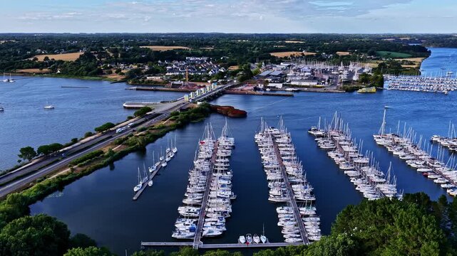 Aerial sideways flight along Port d'Arzal-Camo&euml;l marina showing rows of moored sailboats and river estuary bridge