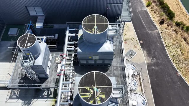 Aerial top down view shows multiple industrial cooling fans with mesh guards on dairy factory rooftop beside road and water