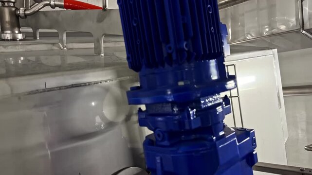 Close up of blue electric motor driving stainless steel mixer inside dairy processing factory with red hose fitting nearby