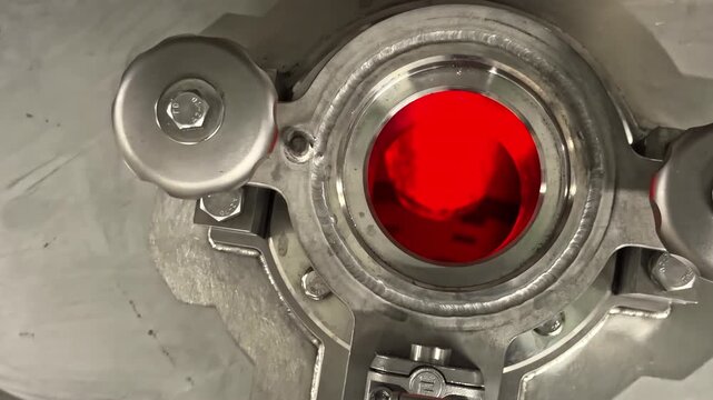 Push in close up shows stainless steel valve with red sight glass and pipe fitting inside dairy processing factory