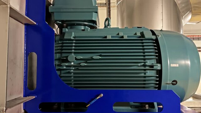 Slow push in reveals large industrial electric motor with cooling fins mounted on blue steel frame inside factory building