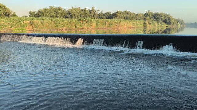 Fast-flowing water rushing over a small dam structure, creating white foam, turbulent currents, and dynamic cascades that highlight the power and movement of flowing water
