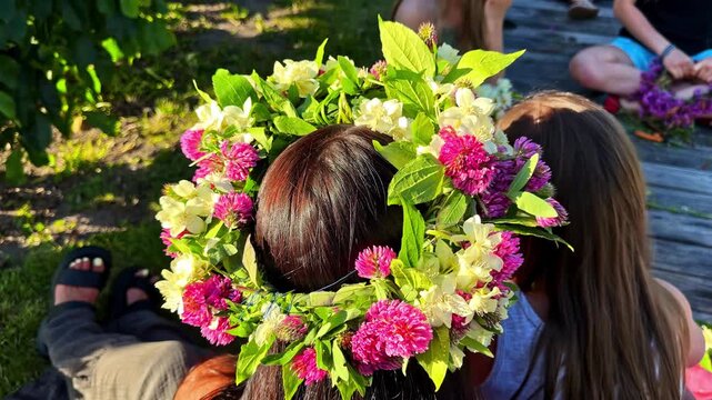 Close-up back view shows woman wearing handmade flower crown with pink clover and white blossoms during summer midsummer festival celebration outdoors
