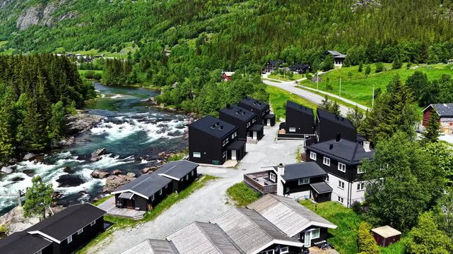 Black Riverside Cabins Sit Beside Rushing Rapids Along the Road From Fl&aring;m to Oslo, Norway - Aerial Drone Shot