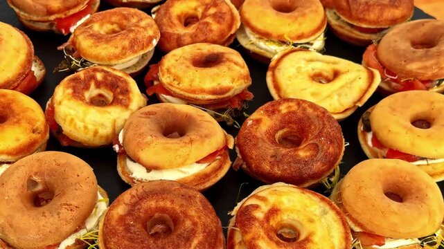 A high angle view showing a large batch of toasted bagel sandwiches filled with cream cheese and savory smoked salmon slices.