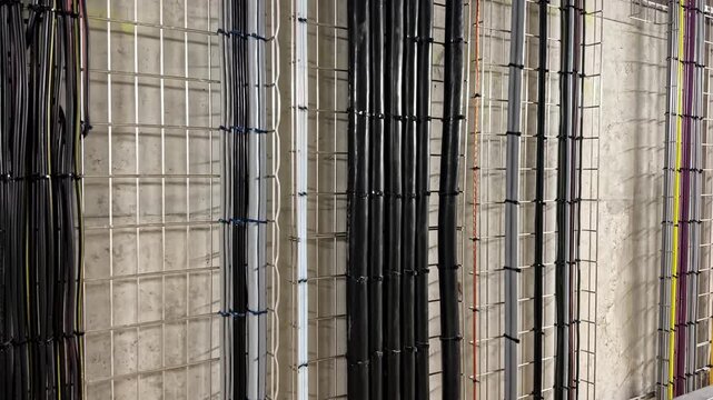 Vertical bundles of color coded electrical conduits run neatly along a concrete wall inside an industrial data facility.